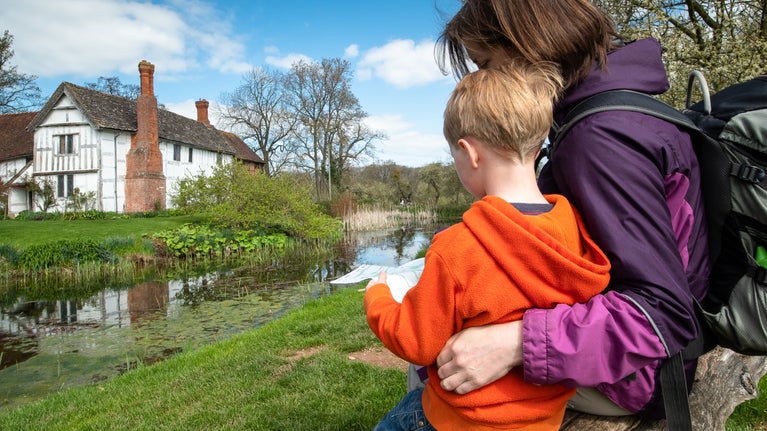 A mother and child sit on a bench overlooking the manor house.